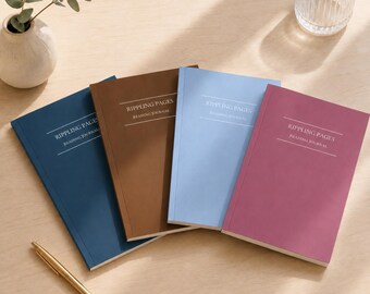 May include: Four rectangular reading journals titled Rippling Pages, arranged in a fan shape. The covers are solid dark blue, brown, light blue, and magenta. Each journal features white text centered on the front cover. A gold pen lies nearby.