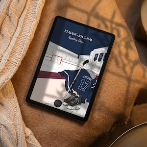 Peut inclure: Une tablette numérique affichant la couverture d'un journal de lecture avec une illustration de patinoire, une crosse de hockey, un palet, des patins et un maillot bleu foncé avec le texte "CAPTAIN 17" et "READING JOURNAL Rippling Pages".