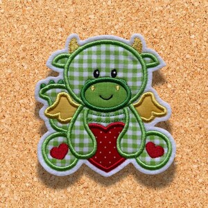 Könnte beinhalten: Grüner und weißer Gingham-Drache, der ein rotes Herz mit weißen Punkten hält. Der Drache hat gelbe Flügel und einen weißen Umriss.