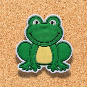 Op de afbeelding: Een groene kikker applicatie met een witte rand en gele buik. De kikker heeft lachende ogen en is gemaakt van stof. De applicatie is ontworpen voor naai- of knutselprojecten. Een klein zebra logo staat in de rechter benedenhoek.