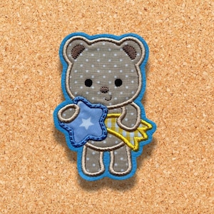 May include: A brown teddy bear with a blue star in its paw, embroidered with white polka dots and a yellow striped scarf. The bear is outlined in blue.