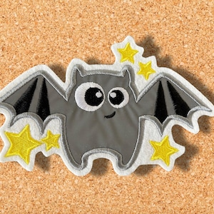 Könnte beinhalten: Eine graue Filzfledermaus mit großen Augen und einem Lächeln, die mit gelben Filzsternen fliegt. Die Fledermaus ist ein süßes und fantasievolles Design, perfekt für ein Halloween-Bastelprojekt.
