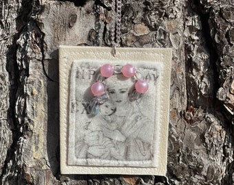 May include: A white leather pendant with a vintage image of a woman and a circle of pink beads around her neck. The pendant is hanging from a silver chain.