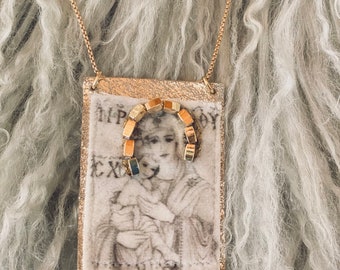 May include: Gold chain necklace with a gold pendant featuring a vintage image of a woman holding a child. The image is framed with a gold border and has the text "EX" and "HP" visible.