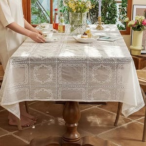 Puede incluir: Un mantel de encaje blanco cubre una mesa de comedor de madera, con vajilla y flores. Dos sillas de madera con asientos de mimbre flanquean la mesa. La habitación tiene un ambiente cálido y acogedor, con luz natural.