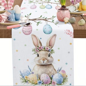 May include: Easter table runner with a watercolour illustration of a bunny wearing a floral crown, surrounded by Easter eggs. The runner has a white background with pastel polka dots and hanging Easter eggs.