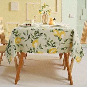 Puede incluir: Un mantel rectangular con un diseño de limones y hojas. El mantel cubre una mesa de madera, complementada con sillas de madera. Un jarrón con limones y un objeto decorativo amarillo están sobre la mesa.