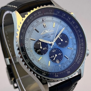 May include: A Breitling Navitimer watch with a blue face and black subdials. The watch has a silver case and a black leather strap. The watch face displays the Breitling logo and the text "1884".