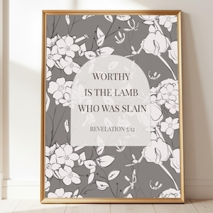 May include: A framed print with a gold border features a floral pattern in white and gray. The text "WORTHY IS THE LAMB WHO WAS SLAIN REVELATION 5:12" is displayed in a white arch shape, creating a decorative wall art piece.