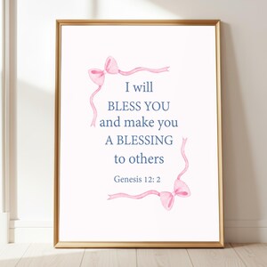Puede incluir: Impresión enmarcada con borde dorado que presenta el texto azul "I will BLESS YOU and make you A BLESSING to others", con el versículo bíblico Génesis 12:2. Lazos rosas de acuarela adornan la parte superior e inferior del texto sobre fondo blanco.