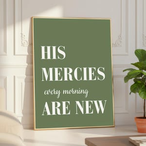 May include: A framed print with a gold border. The background is a solid olive green color. The text in white reads "HIS MERCIES every morning ARE NEW". The print is displayed on a white wall.