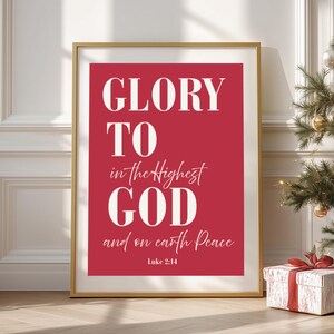 Könnte beinhalten: Ein gerahmter Druck mit den Worten "GLORY TO in the Highest GOD and on earth Peace" in Weiß auf rotem Hintergrund. Der Text stammt aus Lukas 2:14. Der Rahmen ist goldfarben, und ein Weihnachtsbaum und eine Geschenkbox sind im Hintergrund.