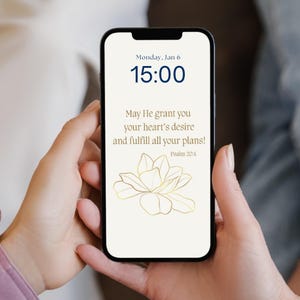 Könnte beinhalten: Ein Smartphone-Bildschirm zeigt den Text "Monday, Jan 6" und "15:00" in Marineblau. Der Bildschirm zeigt auch die Worte "May He grant you your heart's desire and fulfill all your plans!" mit "Psalm 20:4" darunter. Ein goldenes Blumendesign ist ebenfalls sichtbar.