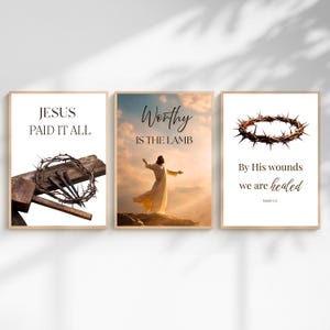 May include: Three framed art prints with religious themes. One features a cross and crown of thorns with the text "JESUS PAID IT ALL." Another shows a figure with outstretched arms and the words "Worthy IS THE LAMB." The third print displays a crown of thorns and the text "By His wounds we are healed."