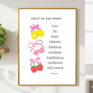 Pode incluir: Uma impressão emoldurada com o texto "FRUIT OF THE SPIRIT" e uma lista de virtudes. A obra de arte apresenta ilustrações de limões, cerejas e morangos, cada uma adornada com laços cor-de-rosa. O texto "Galatians 5" está na parte inferior.