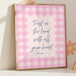 Puede incluir: Arte de pared enmarcado con un fondo de cuadros rosas y blancos. La obra de arte presenta el texto "Trust in the Lord with all your heart" en una fuente cursiva. También se incluye el versículo bíblico Proverbios 3:5.