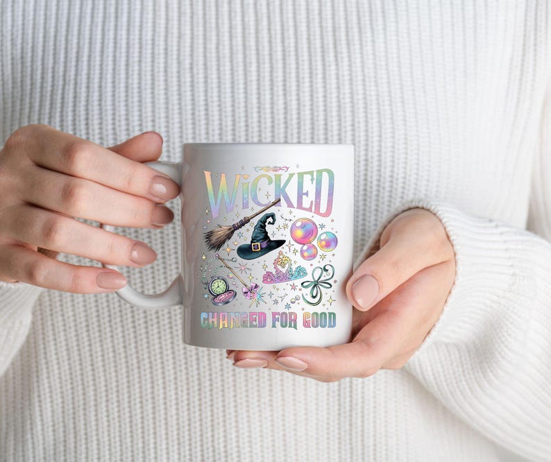 May include: White ceramic mug with the word "WICKED" in iridescent lettering, along with illustrations of a witch's hat, broom, and other magical elements. The phrase "CHANGED FOR GOOD" is printed below the illustrations.
