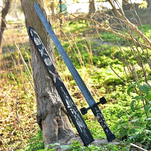 May include: A black and silver sword with a patterned blade and handle, resting against a tree. The sword's sheath is black with silver designs. The blade has a textured pattern.