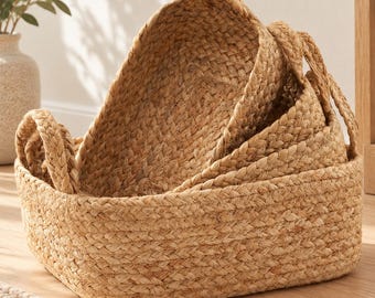 May include: A set of three nested rectangular storage baskets crafted from natural tan braided fibers. Each basket features a thick, woven texture and two integrated side handles, with the baskets stacked inside one another to show their varying sizes.