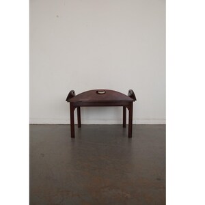 May include: A dark brown wooden serving table with a curved top and a handle in the center. The table has four straight legs and two curved handles on each side. The table is made of wood and has a smooth finish.