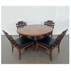 May include: A round wooden dining table with four chairs. The table has a dark wood finish and a decorative metal base. The chairs have black leather seats and woven black straps on the backs.
