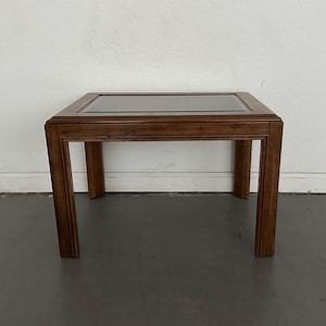 May include: A square, wooden side table with a dark brown finish. The table features a glass top and four sturdy legs. The design is simple and classic, suitable for various interior styles. The table measures approximately 24 inches in height.