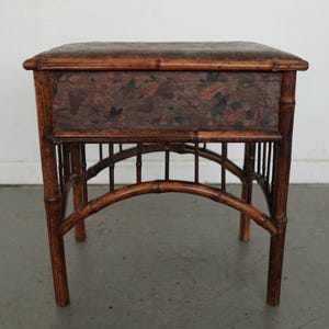 May include: A small, antique bamboo side table with a rectangular top and a drawer. The drawer front features a floral pattern in shades of red, brown, and black. The table has a dark brown finish and a curved bamboo base.