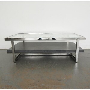 May include: A modern coffee table with a rectangular glass top and a lower shelf. The frame is made of polished metal, and the lower shelf is a dark gray color. The table has a minimalist design and is suitable for a living room.
