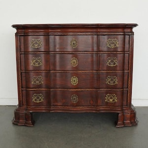 May include: A dark brown wooden chest of drawers featuring four horizontal drawers with curved fronts. Each drawer is equipped with two ornate brass handles and a central brass keyhole escutcheon. The piece stands on four carved feet.