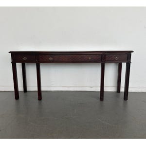 May include: A long, dark brown wooden console table featuring three drawers across the front. The drawer fronts display a textured, diamond-patterned inlay. Each drawer is equipped with a small, curved brass pull handle. The table stands on four straight legs.