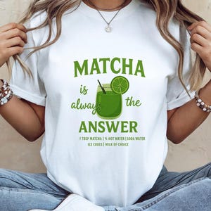 Könnte beinhalten: Weißes T-Shirt mit einem grünen Aufdruck, der lautet: "MATCHA is always the ANSWER". Die Grafik zeigt eine Matcha-Getränke-Illustration mit einer Limettenscheibe. Die Zutaten sind darunter aufgelistet.