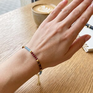 Delicato bracciale di perline di granato, topazio blu di Londra e labradorite da 2-3 mm. Un raffinato gioiello impilabile con pietre preziose naturali e dettagli in oro.