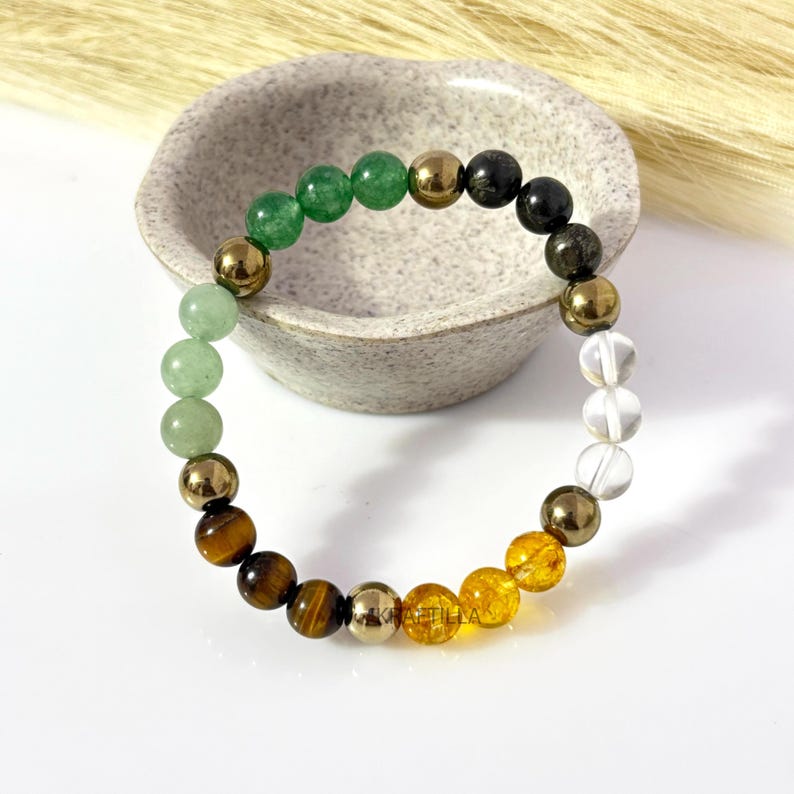 May include: A multi-gemstone bracelet with green, brown, and clear beads, interspersed with gold-coloured pyrite beads. The bracelet is displayed on a white surface. The bracelet's beads include green aventurine and tiger's eye.