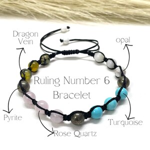 May include: A handmade bracelet with a black cord, featuring beads of various colors and textures. The bracelet includes Dragon Vein, Pyrite, Rose Quartz, Turquoise, and Opal stones. The text on the image reads "Ruling Number 6 Bracelet."
