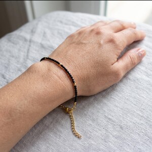 Peut inclure: Un bracelet délicat composé de petites perles noires à facettes alternées avec de minuscules sphères en métal doré. Le bracelet est doté d'un fermoir mousqueton en métal doré et d'une chaînette d'extension réglable.
