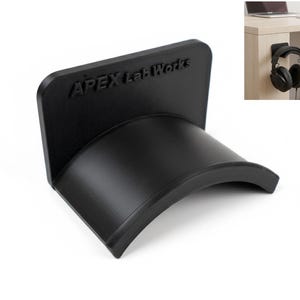 May include: A black headphone stand with the text "APEX Lab Works" embossed on the back. The stand has a curved cradle to hold headphones and a flat back for mounting. The stand is shown with a pair of black headphones.