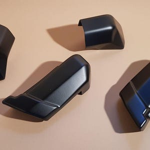 Może przedstawiać: Cztery czarne części samochodowe ułożone na neutralnej powierzchni. Części mają geometryczny kształt z kątowymi powierzchniami i błyszczącym wykończeniem. Części wydają się być nowe i nieużywane.