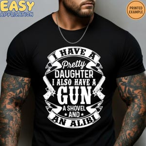 May include: Black t-shirt with a white graphic. The graphic reads "I HAVE A Pretty DAUGHTER I ALSO HAVE A GUN A SHOVEL AND AN ALIBI". The shirt also has the words "EASY APPLICATION" and "PRINTED EXAMPLE".