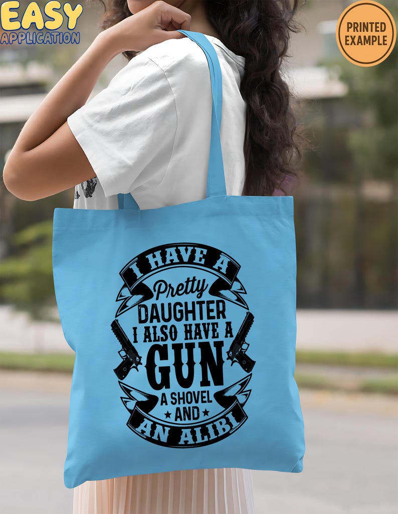May include: A light blue tote bag with the text "I HAVE A Pretty DAUGHTER I ALSO HAVE A GUN A SHOVEL AND AN ALIBI" in a black and white design. The bag also features two gun illustrations. The words "EASY APPLICATION" and "PRINTED EXAMPLE" are also visible.