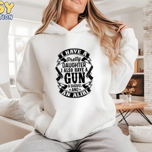 May include: White hoodie with the text "I HAVE A Pretty DAUGHTER I ALSO HAVE A GUN A SHOVEL AND AN ALIBI" in a black design. The design includes two guns and a shovel.