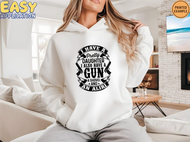 May include: White hoodie with the text "I HAVE A Pretty DAUGHTER I ALSO HAVE A GUN A SHOVEL AND AN ALIBI" in a black design. The design includes two guns and a shovel.
