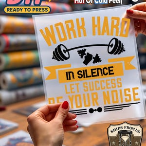 May include: A clear DTF (Direct to Film) transfer sheet with the text "WORK HARD IN SILENCE LET SUCCESS BE YOUR NOISE" in yellow and black. The design includes a barbell and dumbbells. The sheet is held by a person with red nail polish.