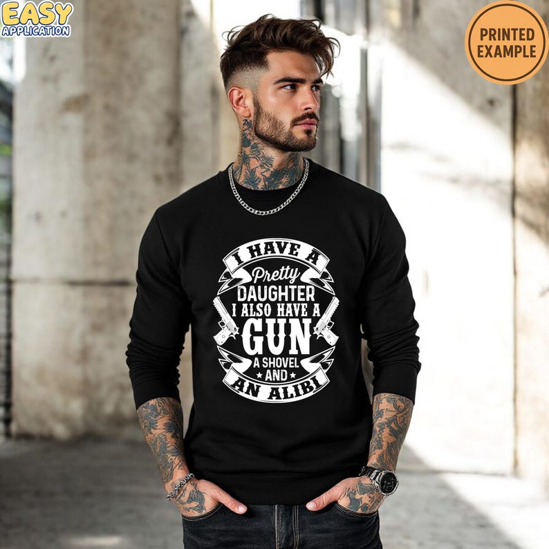 May include: Black long-sleeve sweatshirt with the text "I HAVE A Pretty DAUGHTER I ALSO HAVE A GUN A SHOVEL AND AN ALIBI" in white. The design includes two guns and a shovel graphic. The words "PRINTED EXAMPLE" are in a circle in the upper right corner.