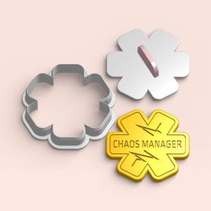 Puede incluir: Tres cortadores de galletas con forma de estrella de seis puntas. Uno es un contorno gris, otro es blanco con un mango rosa y el tercero es dorado con el texto "CHAOS MANAGER" y un gráfico de latido cardíaco.