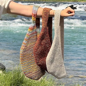 Puede incluir: Tres bolsos de hombro de punto, alineados y sostenidos por un brazo. Los bolsos son de diferentes colores: un patrón de arcoíris a rayas, un marrón liso y un beige liso. Los bolsos están hechos de un material de punto texturizado.