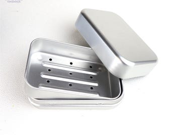May include: A rectangular silver-colored metal soap dish with a removable lid. The base features three raised horizontal ridges with small drainage holes, and the lid is smooth and plain. The brand name herbreeze HANDMADE is visible.