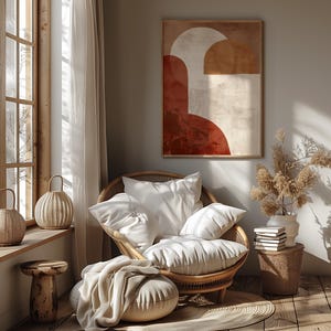 May include: A comfortable living room scene with a rattan chair and white cushions, a framed abstract artwork in warm colours, and a small side table. Natural light streams through a window, creating a relaxing atmosphere.