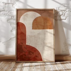 May include: Framed abstract art print with a wooden frame. The artwork uses geometric shapes in rust, beige, and white. The design includes semi-circles and rectangular forms, creating a modern, minimalist aesthetic. The print is displayed against a white brick wall.