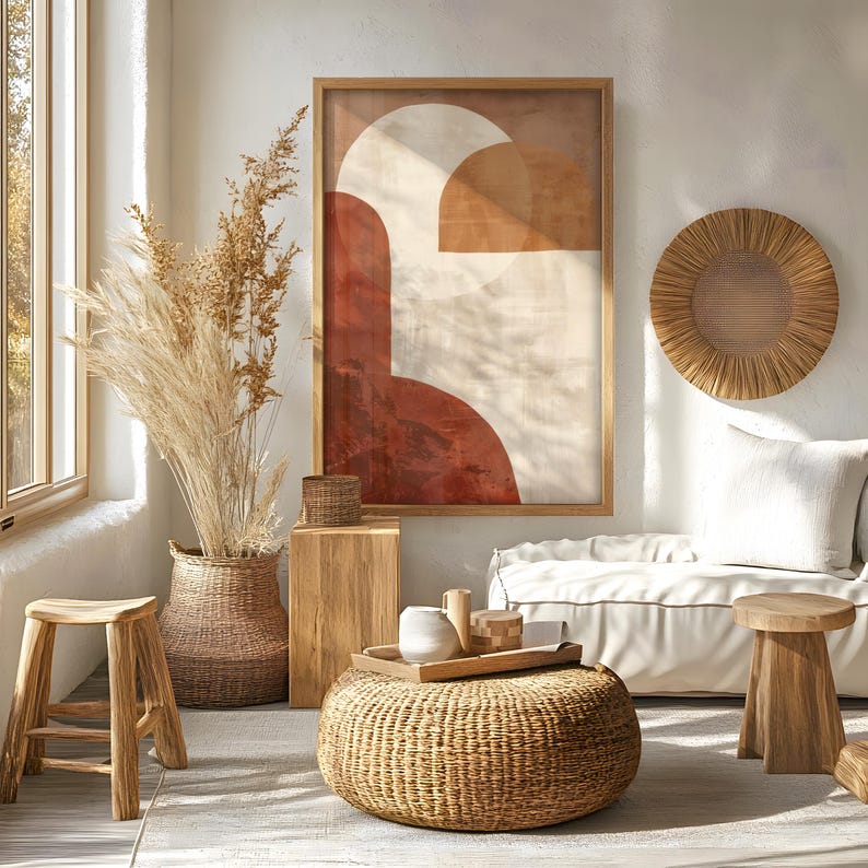 May include: A living room interior with a large framed abstract artwork in red, beige, and white. The room includes a woven coffee table, wooden stools, a wicker basket with tall dried plants, and a woven wall hanging.