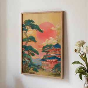 Puede incluir: Impresión artística enmarcada que representa un paisaje japonés. La obra muestra un sol rojo poniéndose sobre una pagoda con tejados azules y paredes rojas, rodeada de árboles verdes. La impresión está enmarcada en un marco de madera marrón claro.